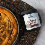 Top view of Halloween Vanilla Bean Cheesecake on the side. Surrounding the cheesecake is halloween scarf and Rodelle 8oz gourmet baking cocoa in a canister.