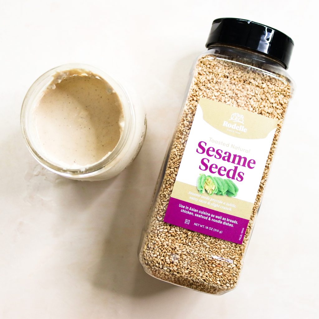 recipe image of Rodelle 18oz sesame seeds laying flat on the table and in the upper left is a mason jar with homemade tahini sauce