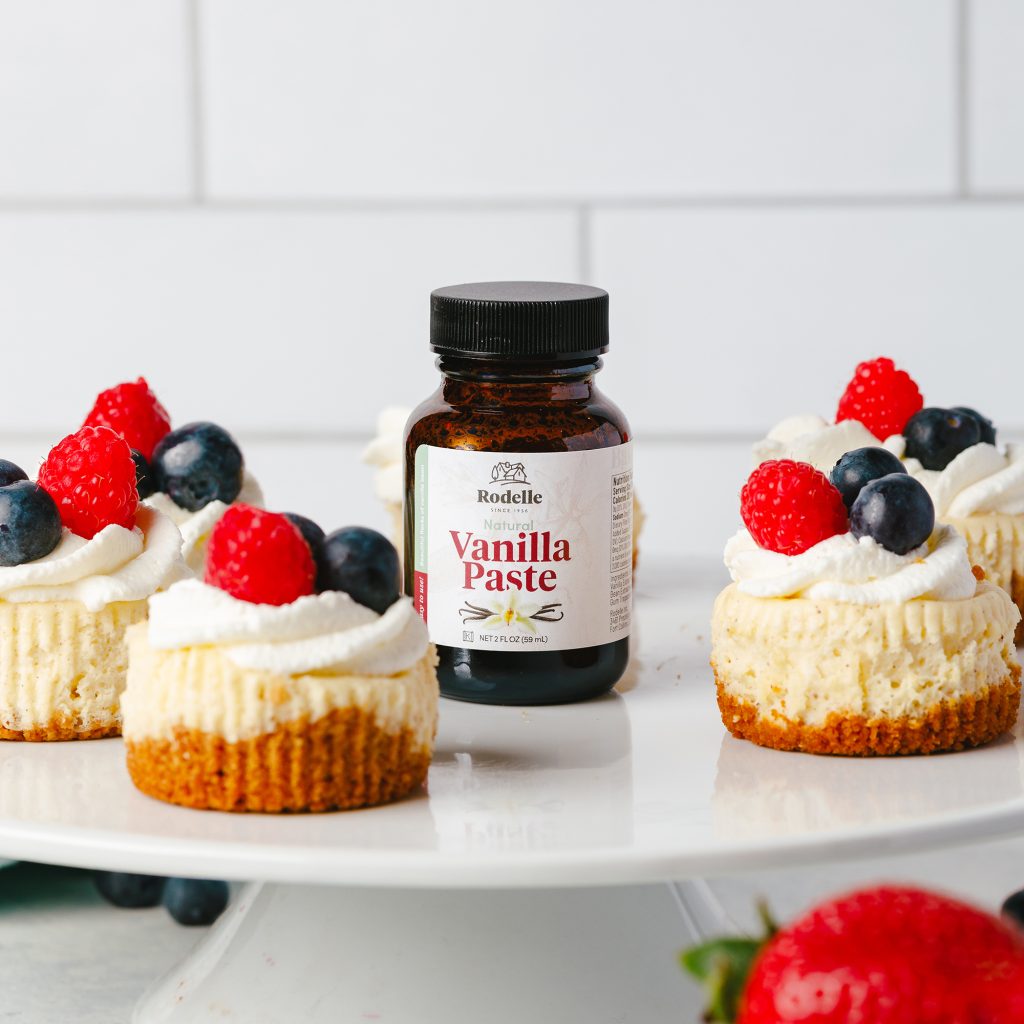 recipe image of mini vanilla bean cheesecakes on a white cake platter. in the center of the mini cheesecakes was rodelle 2oz natural vanilla bean paste