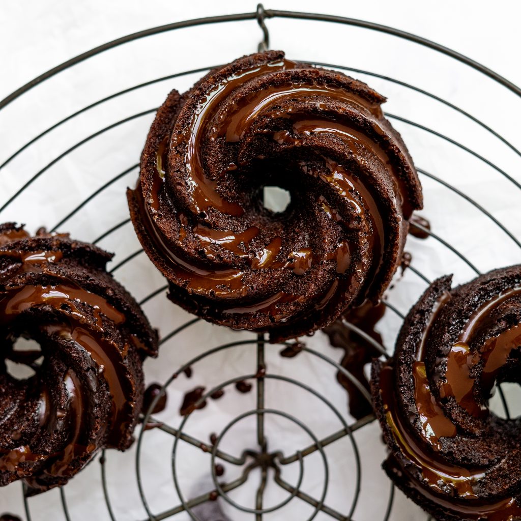 lifestyle image of Chocolate Bundtlettes with Mocha Espresso Glaze. A close up image of them so you can see the texture of the bundlettes and the glaze on top of them. The bundtlettes are on a round black cooling rack
