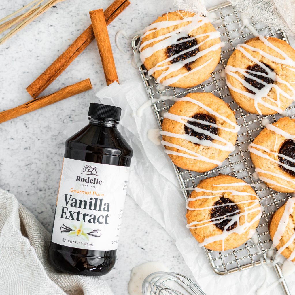 lifestyle image of Vanilla Fig Thumbprint Cookies on a small silver cooling rack. In the upper left are cinnamon sticks and to the bottom left is Rodelle's 8oz gourmet pure vanilla extract bottle