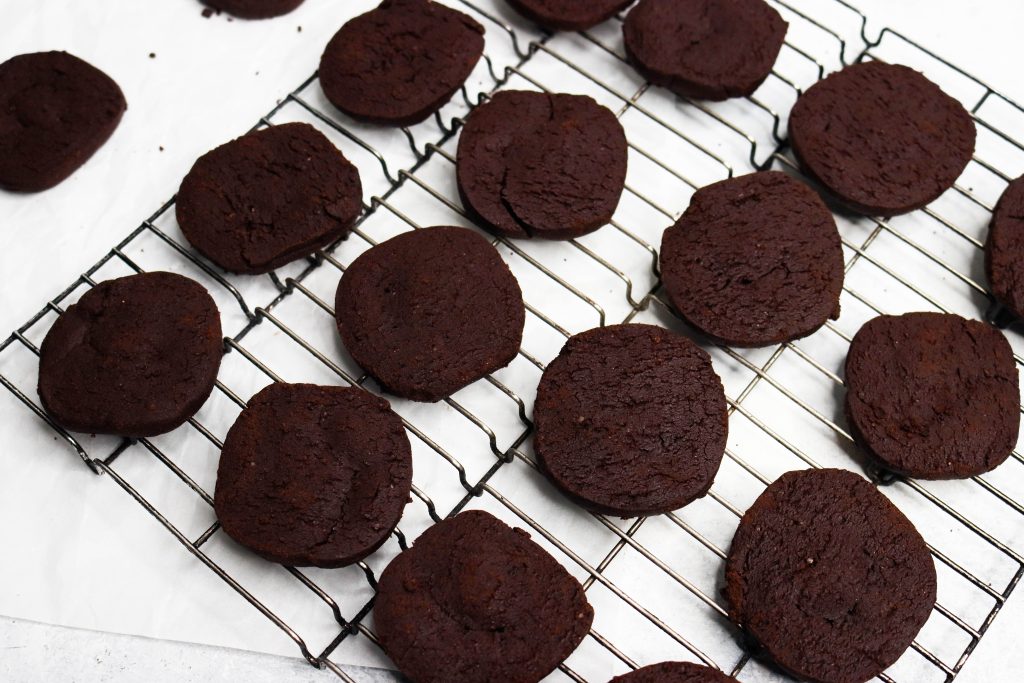 lifestyle image of chocolate shortbread cookies laying on a black cooling rack with white parchment paper/background