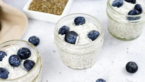 close up of small mason jars containing chia seed pudding and topped with blueberries and coconut flakes.