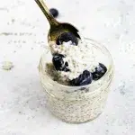 Spoon picking up chia seed pudding with blueberries and coconut flakes from small mason jar.