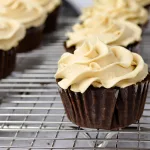 Mocha cupcakes with espresso buttercream piped on top of them. They lay on a cooling wrack.