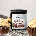 vertical image of Rodelle Gourmet Baking cocoa laying on a cooling wrack surrounded by mocha cupcakes with espresso buttercream