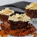 Mocha cupcake cut in half and unwrapped from muffin cup. In the background are mocha cupcakes and a gray striped cloth