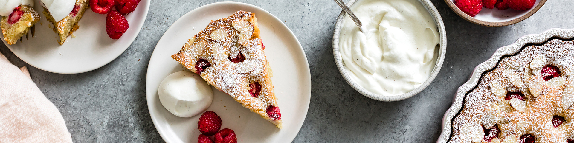 Finished product of the raspberry almond cake on counter plated nicely with cream and berries