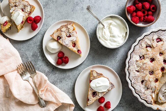 Finished product of the raspberry almond cake on counter plated nicely with cream and berries