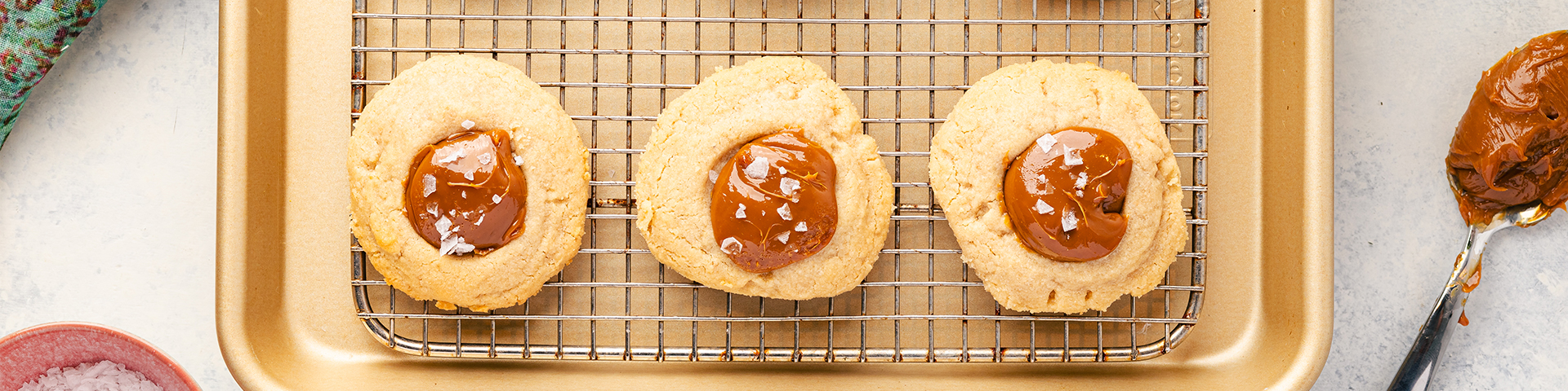 salted dolce de leche thumbprint cookies on cooking rack and baking sheet
