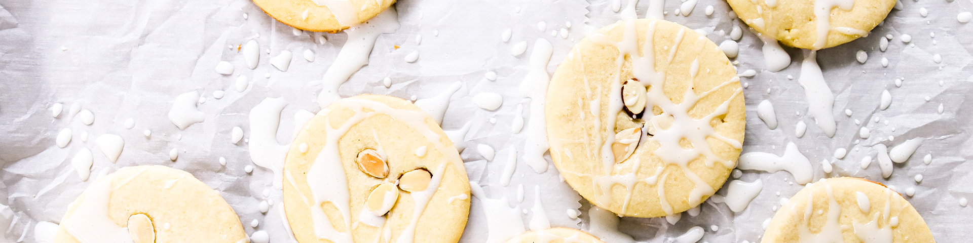 several simple almond cookies on parchment paper background shown from overhead angle with a generous drizzle of white confectioners sugar almond glaze and slivered almonds