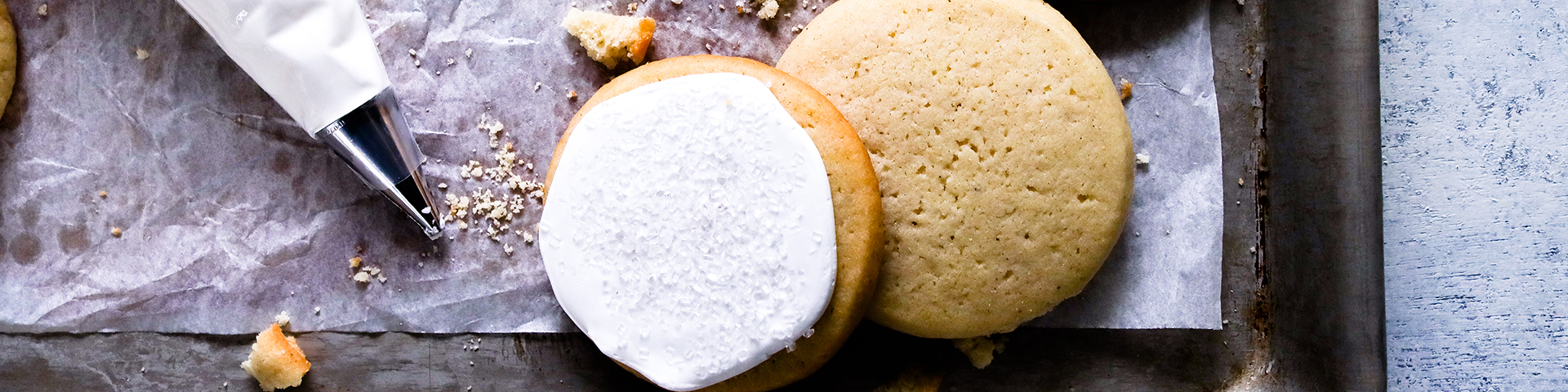 Softest Fluffiest Vanilla Sugar Cookies shown on parchment on cooking tray with frosting bag and some cookie crumbs from overhead angle