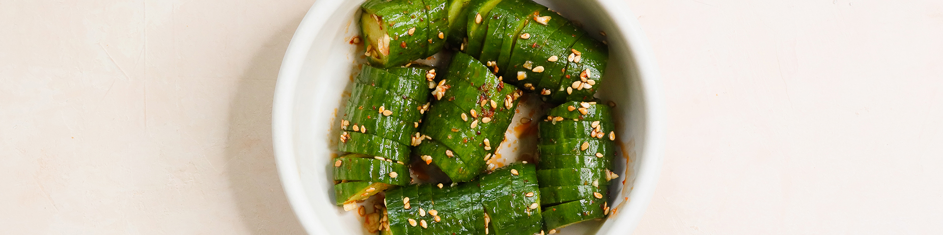 top view of a bowl of sliced spicy asian cucumber salad with chili crunch and neutral background
