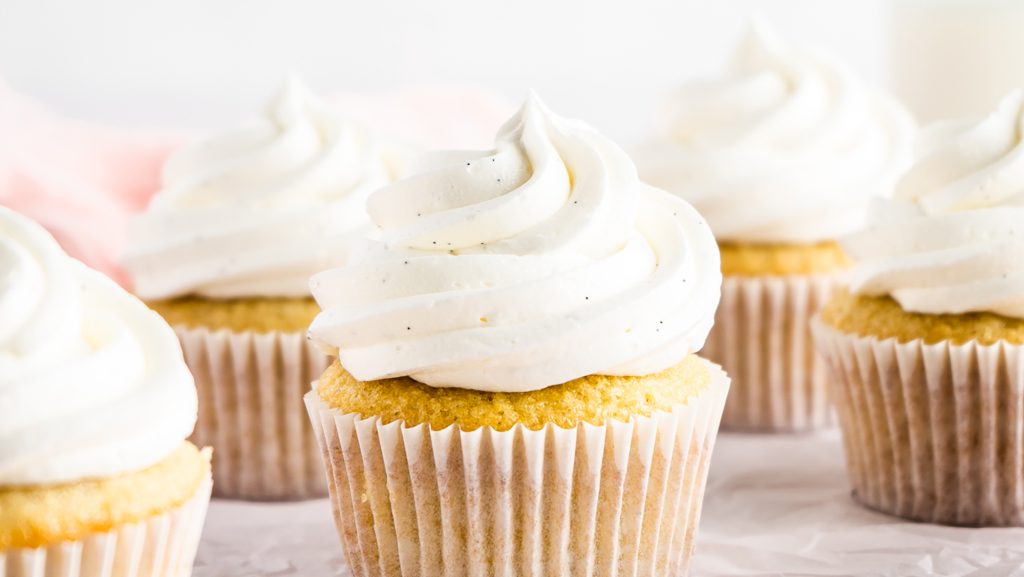 close up shot of vanilla cupcakes with a tall vanilla bean buttercream where you can see the fleck of vanilla seeds scattered within the frosting.