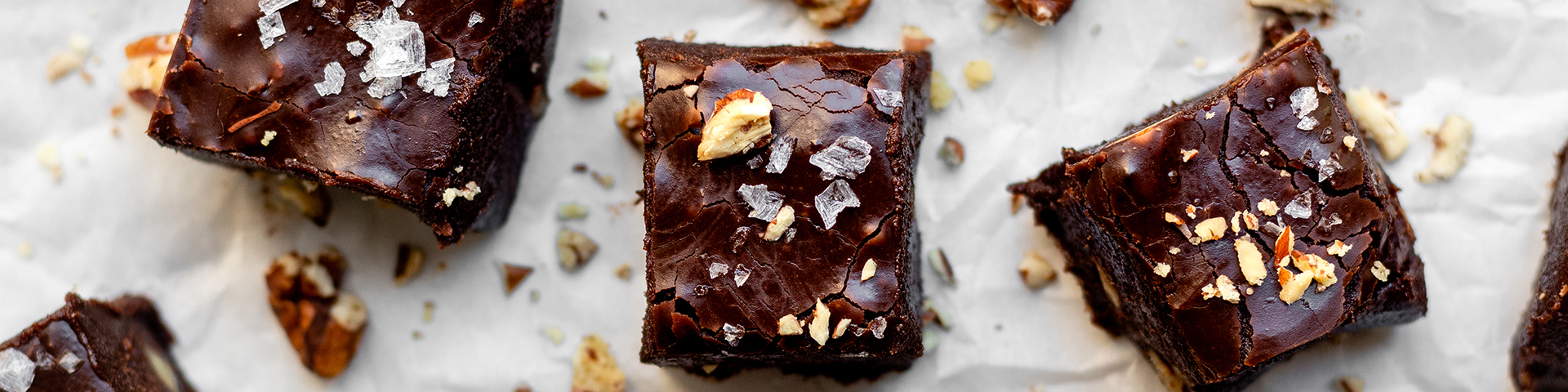 squares of dark chocolate fudge on parchment paper with sea salt and pecans