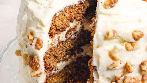 Close up of whole layered carrot cake with a slice of cake taken out.