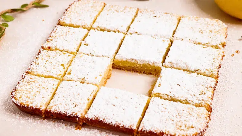 Lemon bars cut into squares to create 16 pieces. One lemon bar missing from whole set.