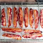 Top shot of vanilla candied bacon laying on top of cooling rack with metal sheet pan with parchment paper below.