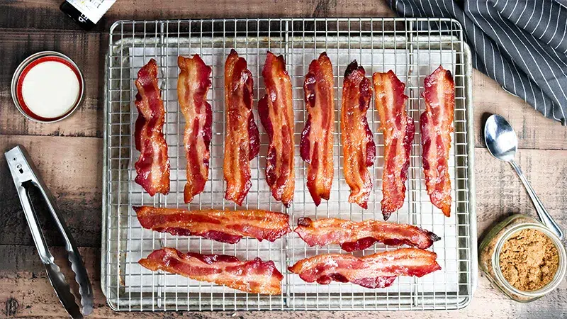 Vanilla Bourbon Candied Bacon Top shot of vanilla candied bacon laying on top of cooling rack with metal sheet pan with parchment paper below.