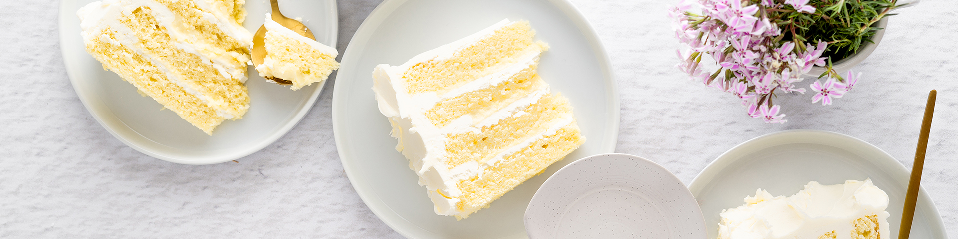 Slices of Vanilla Yuzu Layer Cake on individual plates with spoons and some bites removed to show texture