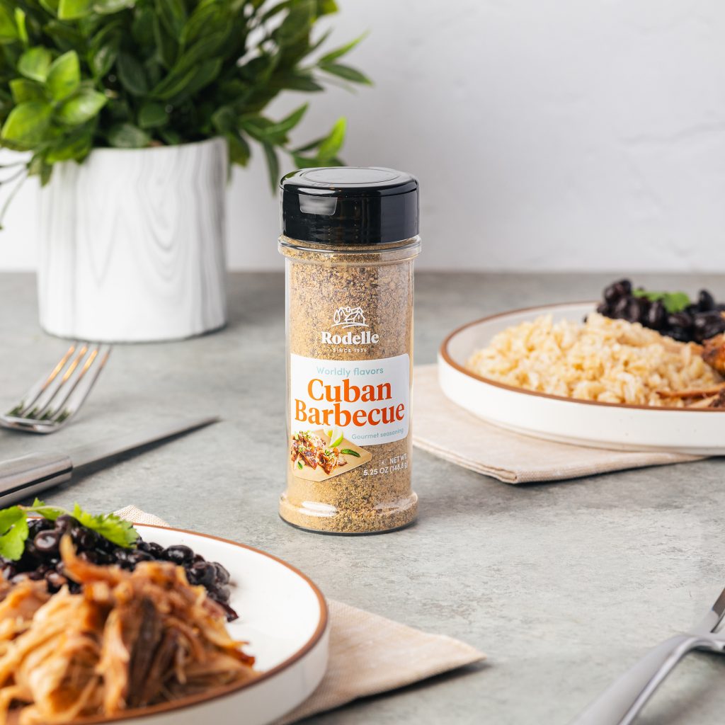 lifestlye shot of Rodelle's cuban barbecue seasoning being poured onto a plate. The bacgkround is white tile and the table is a light marble gray pattern.