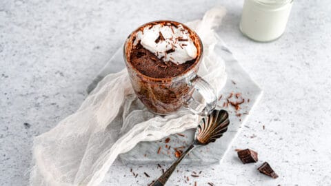 Flourless dark chocolate mug cake in glass mug on neutral background with spoon