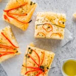 Baked Foccacia with herbs and vegetables on it displayed on neutral background