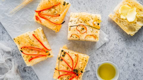 Baked Foccacia with herbs and vegetables on it displayed on neutral background