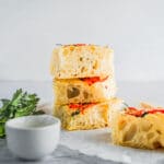 Baked Foccacia with herbs and vegetables on it displayed on neutral background