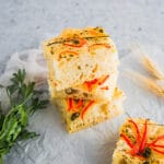 Baked Foccacia with herbs and vegetables on it displayed on neutral background