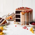 Brownie layer cake with caramel drip and seasonal fall fruits on a neutral background