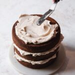 Brownie layer cake being frosted on a neutral background