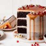 Sliced Brownie layer cake with caramel drip and seasonal fall fruits on a neutral background