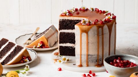 Sliced Brownie layer cake with caramel drip and seasonal fall fruits on a neutral background