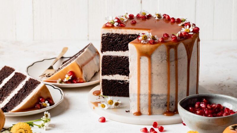 Sliced Brownie layer cake with caramel drip and seasonal fall fruits on a neutral background