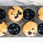 Golden blueberry muffins in muffin tin on neutral background