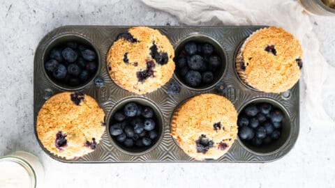 Golden blueberry muffins in muffin tin on neutral background