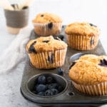 Golden blueberry muffins in muffin tin on neutral background