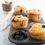 Golden blueberry muffins in muffin tin on neutral background