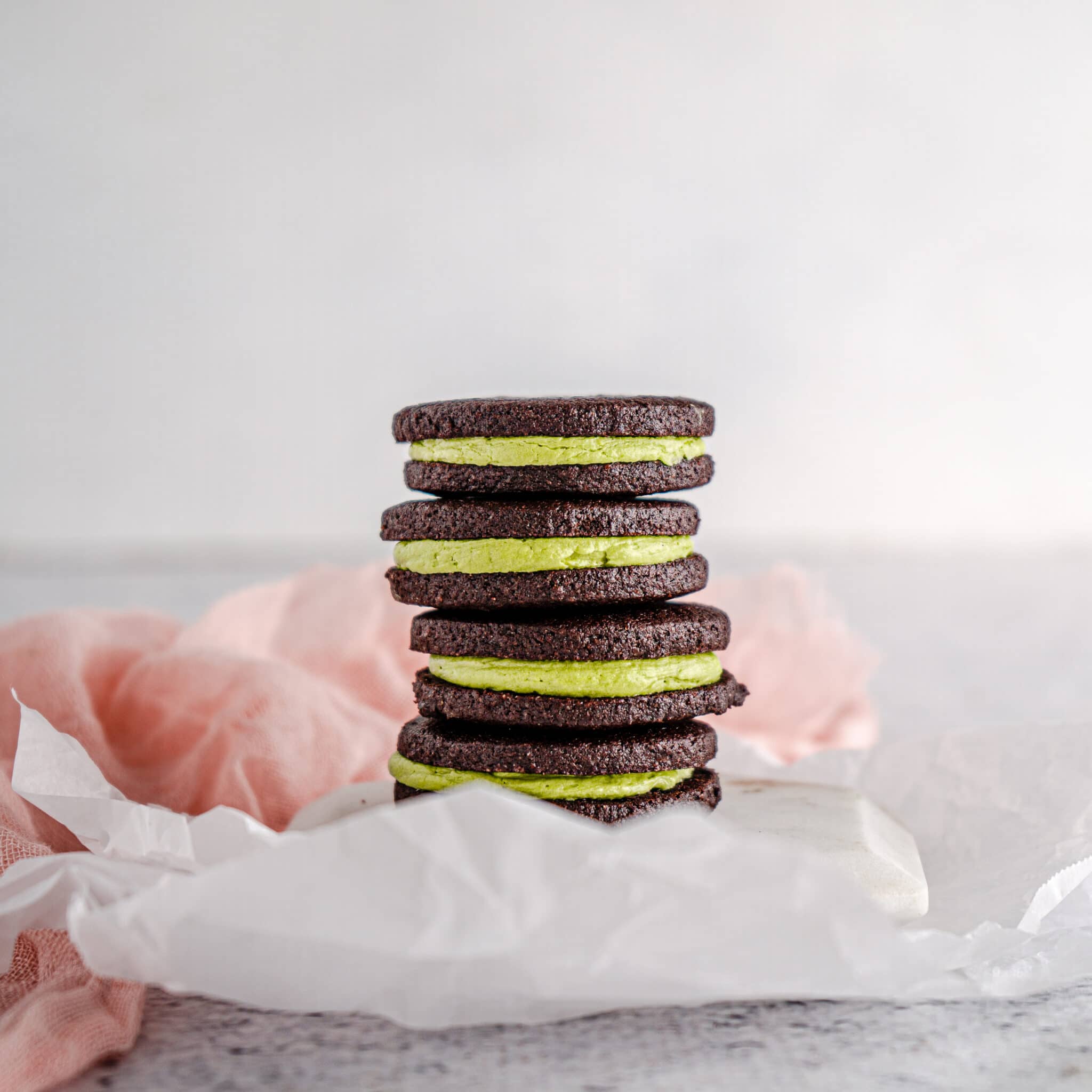 Matcha filled cocoa cookies stacked in a tower on neutral background