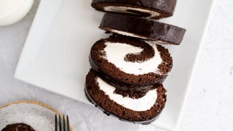 Close up of Swiss roll cake with frosting and ganache on plates with silverware