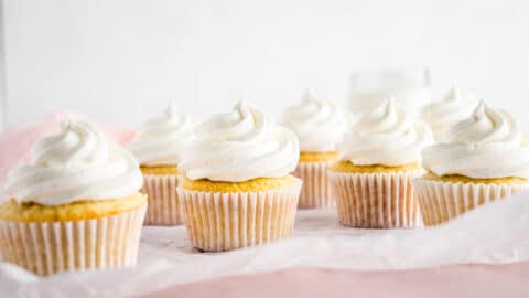 Vanilla cupcakes with vanilla frosting piped on with a pink background