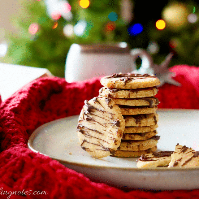 Almond shortbread cookies stacked on plate in front of Christmas tree