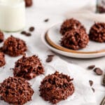Chocolate macaroon cookies on neutral background shown with plate, milk, and serving tools