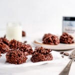 Chocolate macaroon cookies on neutral background shown with plate, milk, and serving tools