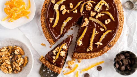 Flourless walnut cake with chocolate glaze on a neutral background with slice being taken out