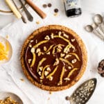 Flourless walnut cake with chocolate glaze on a neutral background with serving utensils and vanilla extract in background