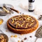 Flourless walnut cake with chocolate glaze on a neutral background with serving utensils and vanilla extract in background