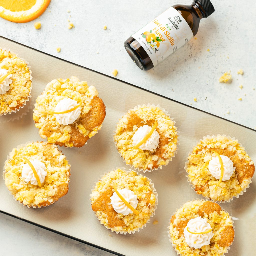 lifestyle recipe image of Orange Vanilla Cream Streusel Muffins on a rectangular white dish with black trim. in the upper right corner is rodelle's fiori di scilia flavor