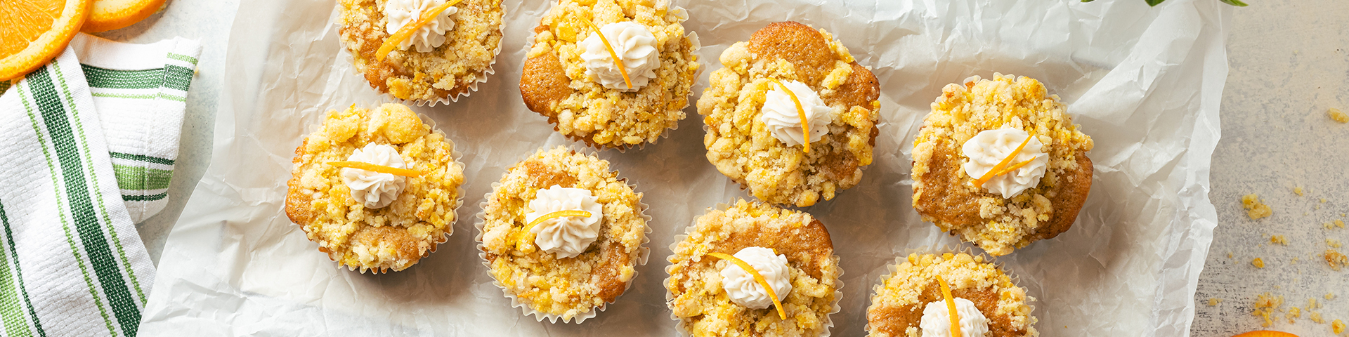 Finished product of orange vanilla cream streusel muffins, shown from overhead angle in muffin pan on marble counter with slices of oranges